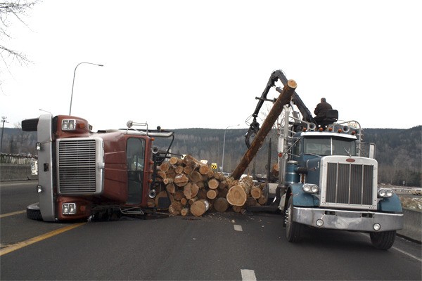 Mike Bartholomew of North Bend picks up logs blocking the center turn lane of the Hwy 202 bridge in Fall City Tuesday morning. The log truck tipped over because a U-bolt in the suspension broke as the southbound truck was turning west onto the roundabout. No one was injured.