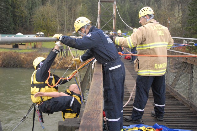 A rescuer with the Eastside Fire & Rescue technical rescue team supports his 'patient' with his legs as fellow rescue team members haul him to the top of the footbridge at Tolt MacDonald Park Friday