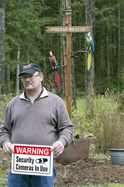 Bob Dawson stands in front of the Macaw Rescue & Sanctuary sign with his new security camera warnings.