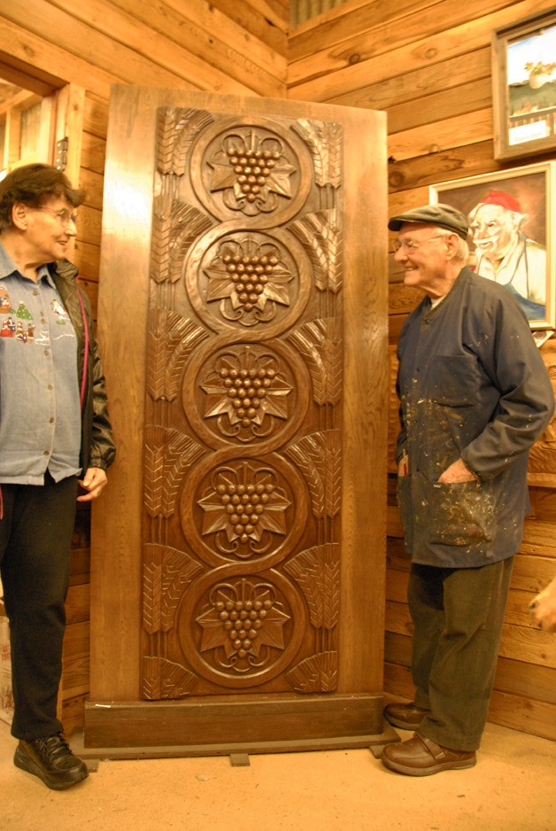 Eva and Adi Hienzsch smile at each other over a custom door that Adi carved by hand. He no longer does this custom work