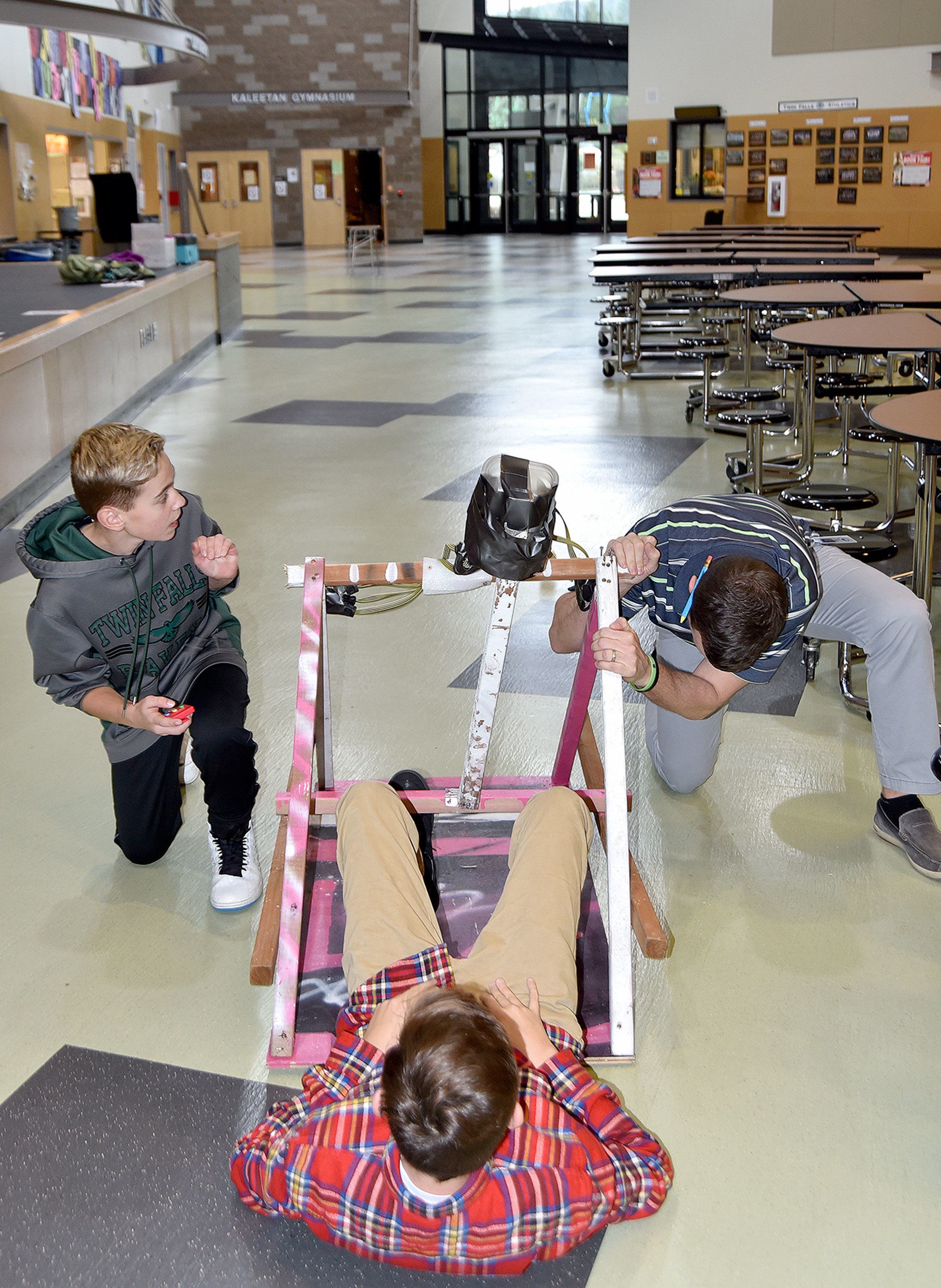 In a final test of their catapult, Carson Netu, left, and Luke Hunter, center, try launching a ball — last year’s catapult project projectile, to compare it to their results with the beanbag, while their teacher Kyle Wallace stabilizes one end of their device.                                Carol Ladwig/Staff Photo
