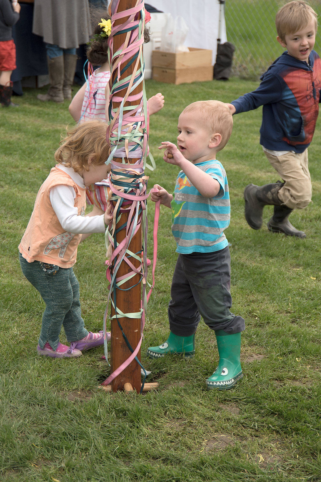 Toddlers Grace Haakenson and Wulfric White, both age 2, examine the Carnation Farmers Market Maypole as their older siblings chase each other around it during opening day festivities, Tuesday, May 2.                                Carol Ladwig/Staff Photo