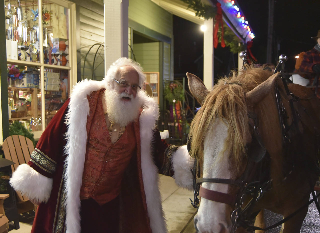 Father Christmas (left) greets one of the hard-working draft horses who pulled wagonloads of visitors through downtown Snoqualmie for hours Saturday during the city’s holiday festivities. Sno Valley Winds musicians Erik Dickerson, center, and Erik Thurston performed for Saturday’s tree lighting in Snoqualmie in holiday themed hats, the Grinch and Santa, respectively. (File Photo)