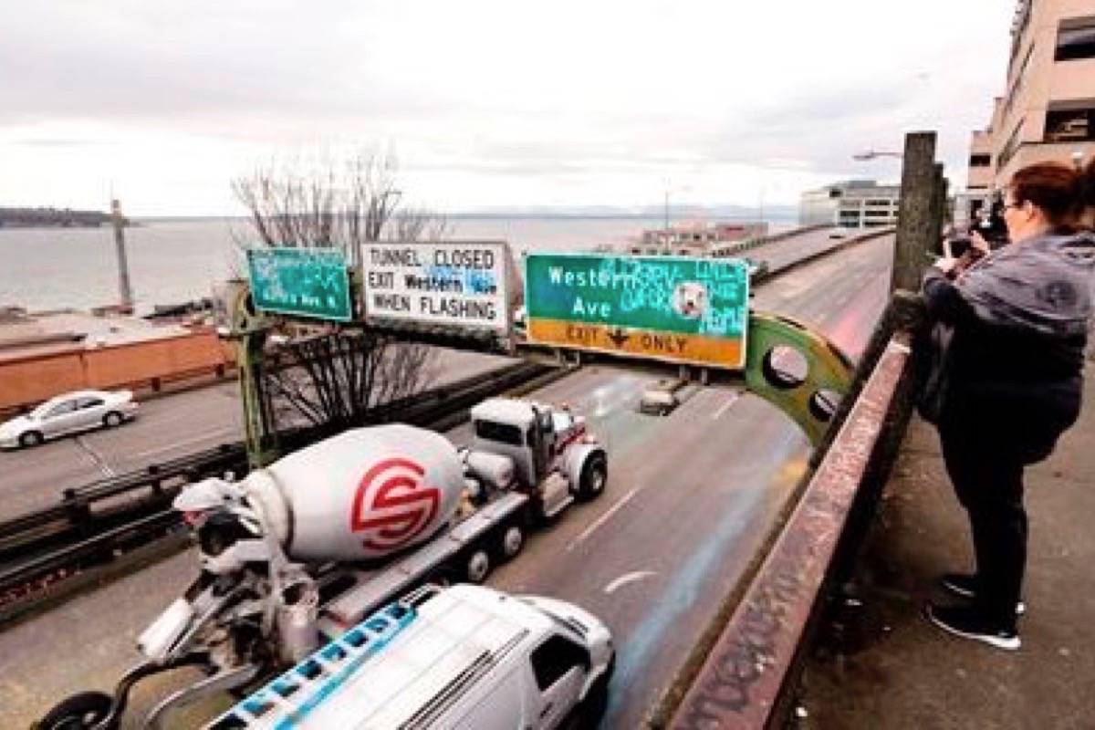 A woman takes a photo toward Elliott Bay as Alaskan Way Viaduct traffic rolls past her below ahead of an upcoming closure of the roadway, in Seattle. (AP Photo/Elaine Thompson)