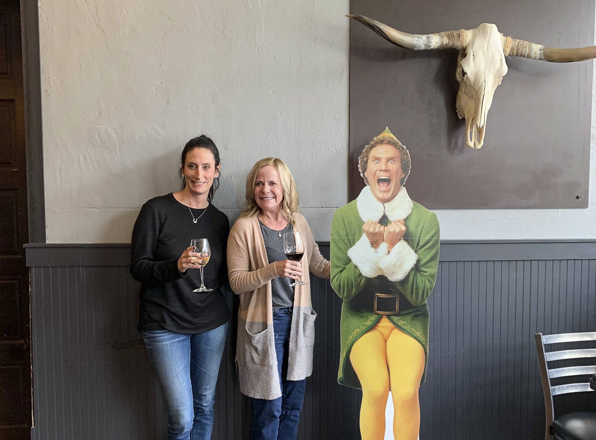 Theresa Nielson (L) and Julie Edwards break from their lunch date to pose for a photo with Buddy the Elf inside The Iron Duck in North Bend. The North Bend Downtown Foundation is encouraging folks to shop local this holiday season. Natalie DeFord/staff photo