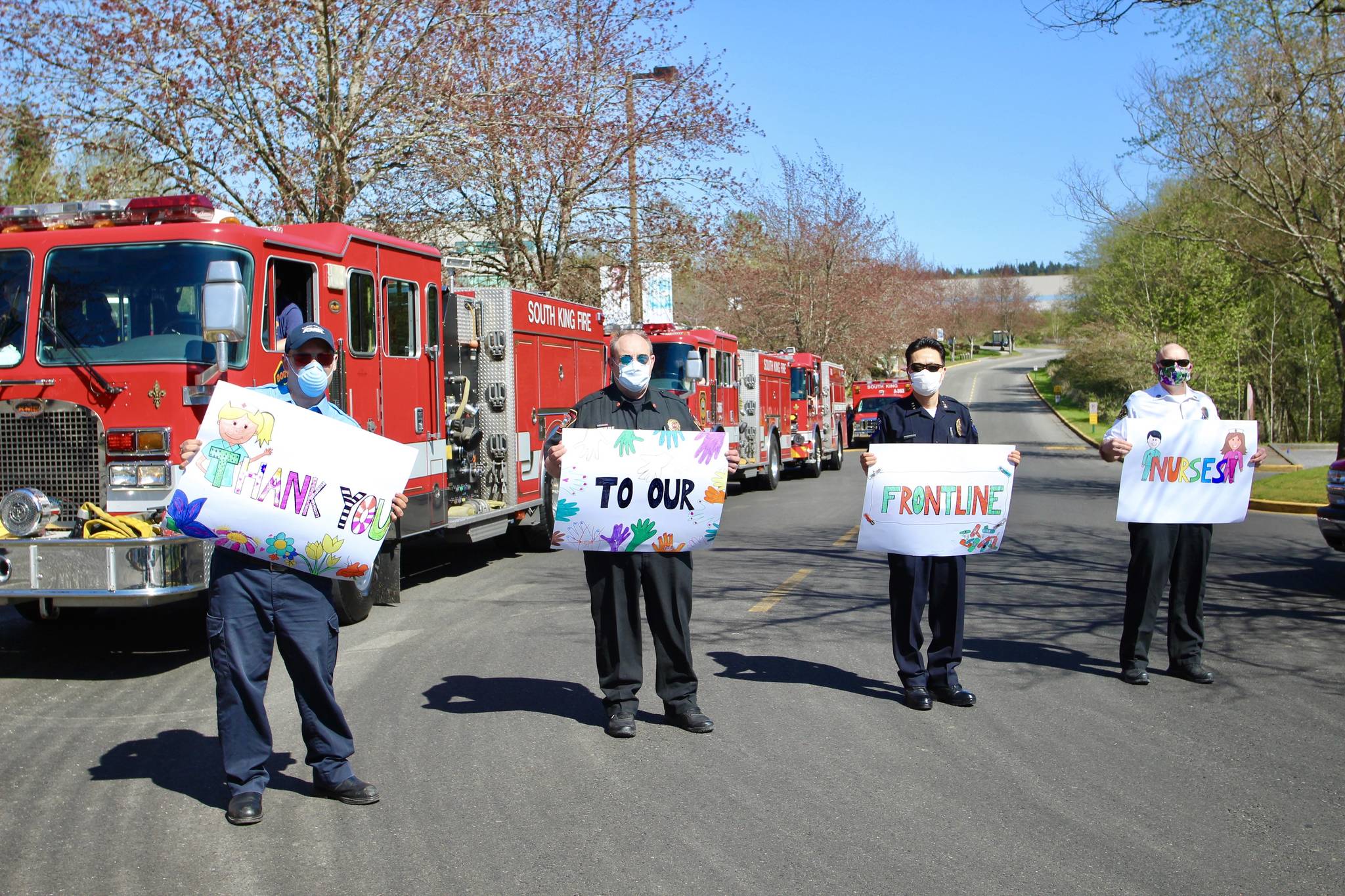 L-R: AMR Supervisor Kevin Devine, SKFR Fire Chief Vic Pennington, Federal Way Police Chief Andy Hwang and King County Medic One Chief Andy Tait hold signs made by Federal Way residents Justin and Darianne Westcott and their kids. Olivia Sullivan/staff photo