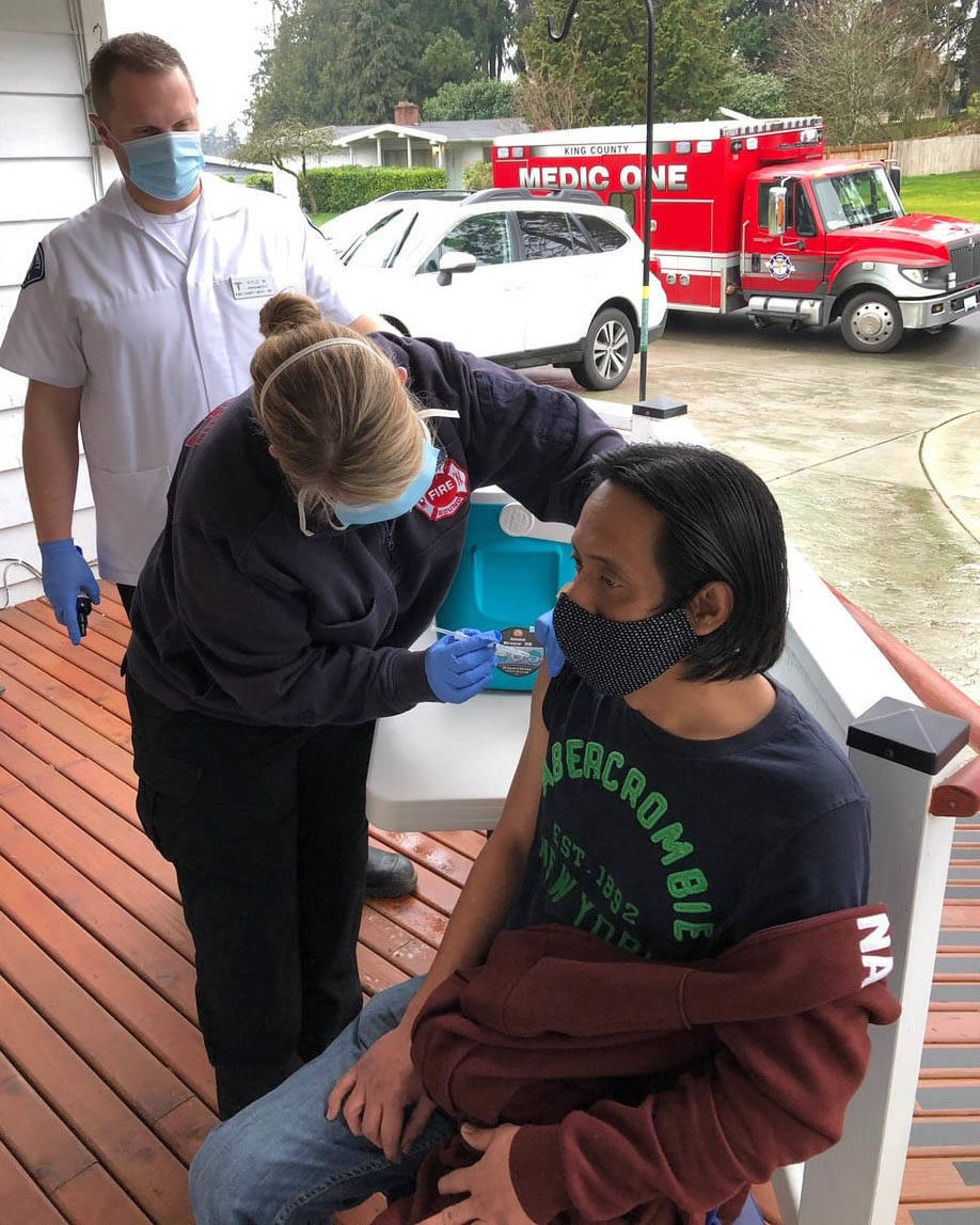 Nurse Sara Hardin, part of Puget Sound Fire’s first COVID-19 mobile vaccination unit, delivers a shot Jan. 21 to a resident at an adult family home in Kent. Kyle Waterman, a King County Medic One paramedic, looks on. COURTESY PHOTO, Puget Sound Fire