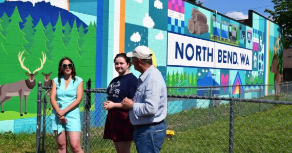 Sarah Hughes, left, unveils her mural in June alongside Ava Mulligan, a Two Rivers High School Student, and North Bend Mayor Rob McFarland. Photo by Conor Wilson/Valley Record.