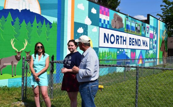 Sarah Hughes, left, unveils her mural in June alongside Ava Mulligan, a Two Rivers High School Student, and North Bend Mayor Rob McFarland. Photo by Conor Wilson/Valley Record.