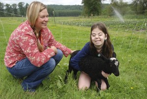 Camper Katherina Goodwin holds a baby lamb and Camp Korey gardener