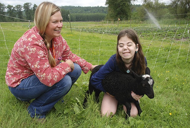 Camper Katherina Goodwin holds a baby lamb and Camp Korey gardener