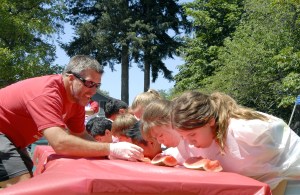 Carol Ladwig/Staff PhotoSean Christensen helps contestants in the 2015 watermelon-eating contest. This year’s contest starts at 1:30 p.m. at Olive Taylor Quigley Park.