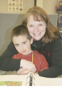 First-grader Trevor Moon sits on teacher Sally Combs’ lap as he works on a journal. Combs’ physical approach is one of the ways she adapts to her students’ autism