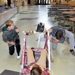 In a final test of their catapult, Carson Netu, left, and Luke Hunter, center, try launching a ball &mdash; last year&rsquo;s catapult project projectile, to compare it to their results with the beanbag, while their teacher Kyle Wallace stabilizes one end of their device.                                Carol Ladwig/Staff Photo