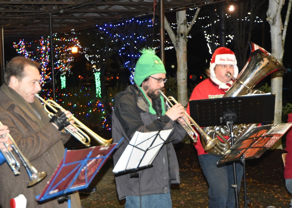 Sno Valley Winds musicians Erik Dickerson, center, and Erik Thurston performed for Saturday&rsquo;s tree lighting in Snoqualmie in holiday themed hats, the Grinch and Santa, respectively.
