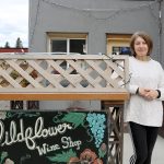 Denise Romary, who co-owns Wildflower Wine Shop with Kimberlea Miller, poses for a photo by the shop sign. Evan Pappas/Staff Photo