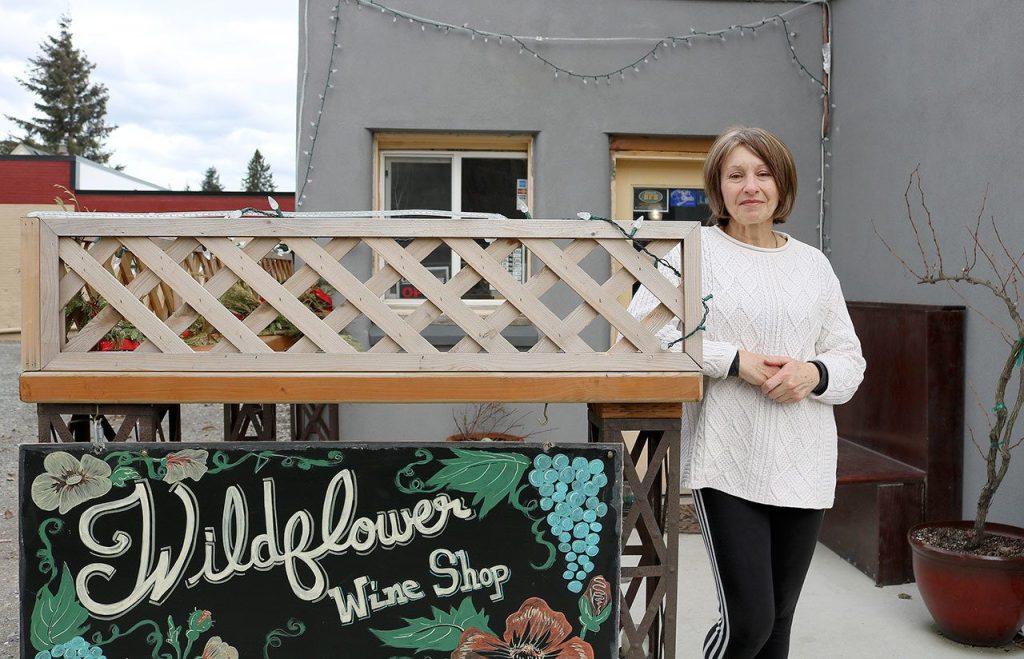 Denise Romary, who co-owns Wildflower Wine Shop with Kimberlea Miller, poses for a photo by the shop sign. Evan Pappas/Staff Photo