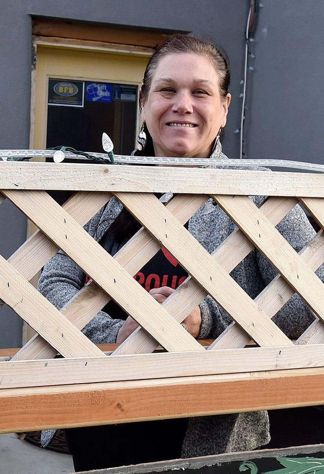 Kimberlea Miller, co-owner of Wildflower Wine Shop, peeks over the lattice surrounding the shop&rsquo;s patio.                                Carol Ladwig/Staff Photo