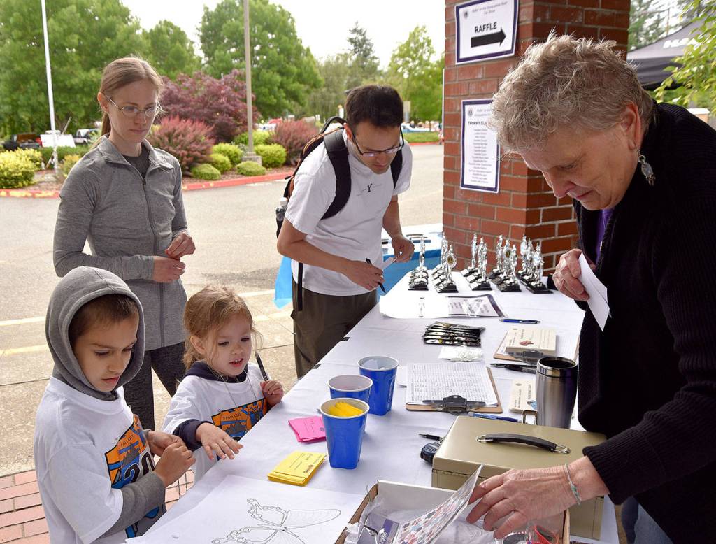 Youngsters Asher and Kira Clark debate their choices in the car show voting, while volunteer Anne Smarsh finds something to reward their efforts. The family, including Amanda and Bryce Clark in the background, had just finished the 1K race before visiting the car show.                                Carol Ladwig/Staff Photo