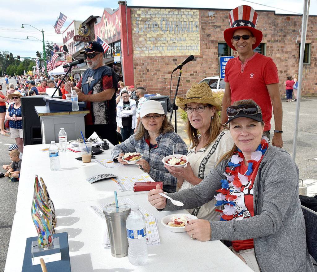 Riverview Schools Committee members Christine Hillstad, Allison Hawkins and Heather Dow enjoy strawberry shortcake as parade MCs Jack Ballard and Stuart Lisk get ready for the parade to start. (Carol Ladwig Staff Photo)