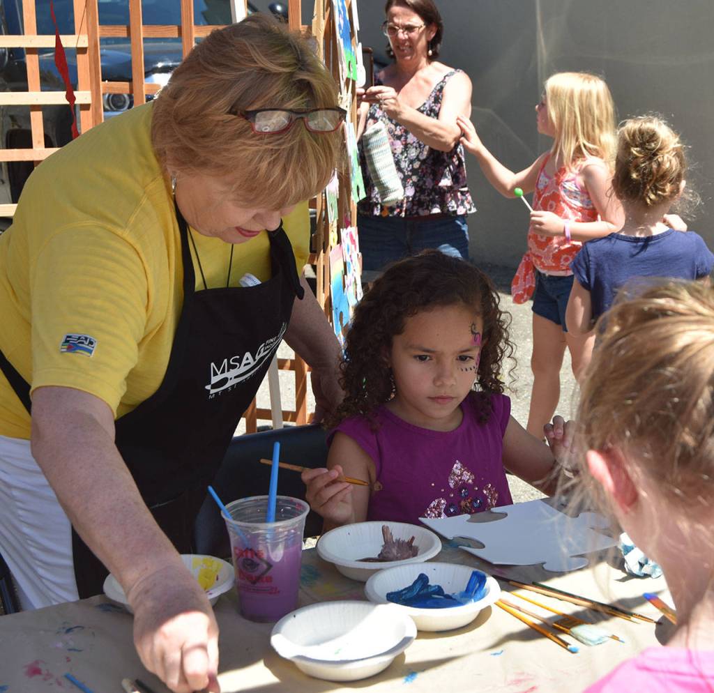 Sara Lewis gets help from a Mount Si Artist Guild volunteer to start painting her masterpiece, a puzzle piece for a community collage. Carol Ladwig/Staff Photo