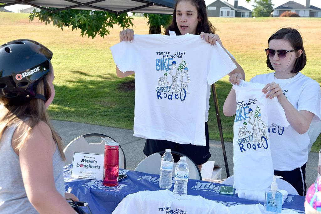 Natalie Tassielli and Hallie Rogers, volunteering at the Tanner Jeans T-shirt station, hold up the free shirts for children who complete the rodeo. Also helping out,but not pictured was Ivy Simon.                                (Carol Ladwig/Staff Photo)