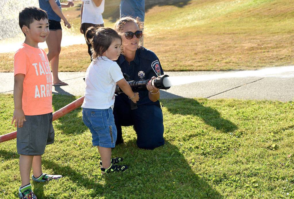 Children lined up to try firefighting for themselves. With a little help from an adult, they used a fire hose to spray out a fire, represented by orange traffic cones.                                (Carol Ladwig/Staff Photo)