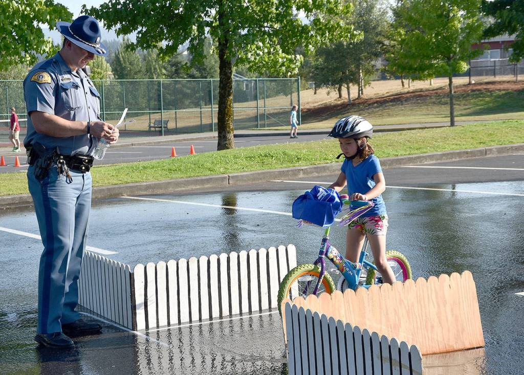 Zoe, age 7, answers questions from Trooper Tim Williams at the four-way stop challenge of the Tanner Jeans Bike Rodeo Aug. 1.                                (Carol Ladwig/Staff Photo)
