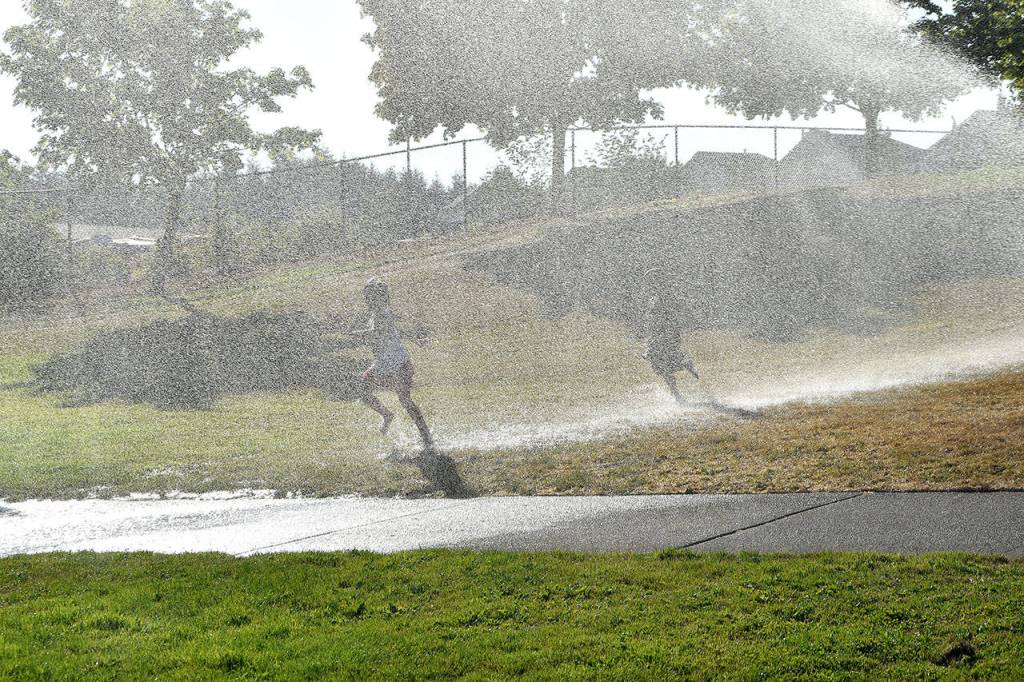 Children take a cooling run through the sprinkler set up courtesy of the Snoqualmie Fire Department.                                (Carol Ladwig/Staff Photo)
