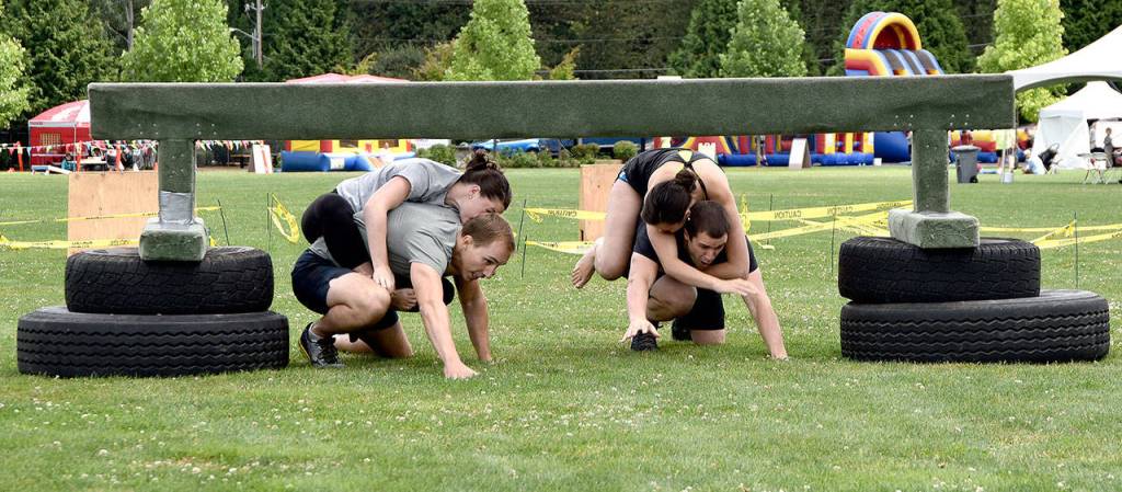 Crawling under a second obstacle, wife-carrying competitors Chris and Jamie Teteak, left, and Pactrick and Faith McKee, right, are evenly matched in the first race of the day Sunday.                                (Carol Ladwig/Staff Photo)
