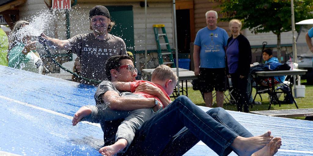 Competitors in the sibling carrying competition get a helpful jet of water to speed them to their finish in a waiting kiddie pool.                                (Carol Ladwig/Staff Photo)