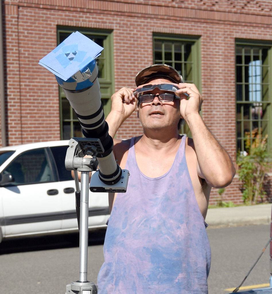 Scott Dodson alternates viewing the eclipse through his heavily-filtered telescope, a pair of eclipse viewers, and a jumbo-size pinhole projecter he created. Dodson brought all his devices Monday morning to Carmichael&rsquo;s Hardware in Snoqualmie, where people gathered to watch the first solar eclipse in the U.S. since 1979.                                (Carol Ladwig/Staff Photo)
