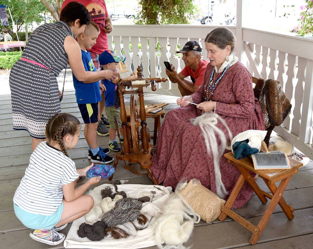 Karen Haas, a historic re-enactor, spins wool into yarn as she welcomes a family with all of their questions about historic life.                                (Carol Ladwig/Staff Photo)