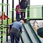 Mayor Matt Larson wipes down the slide so that the waiting Brielle Collins, or possibly Snoqualmie Police Chief Perry Phipps, can try out the new play equipment at Ironwood Park, despite the rain. (Carol Ladwig/Staff Photo)