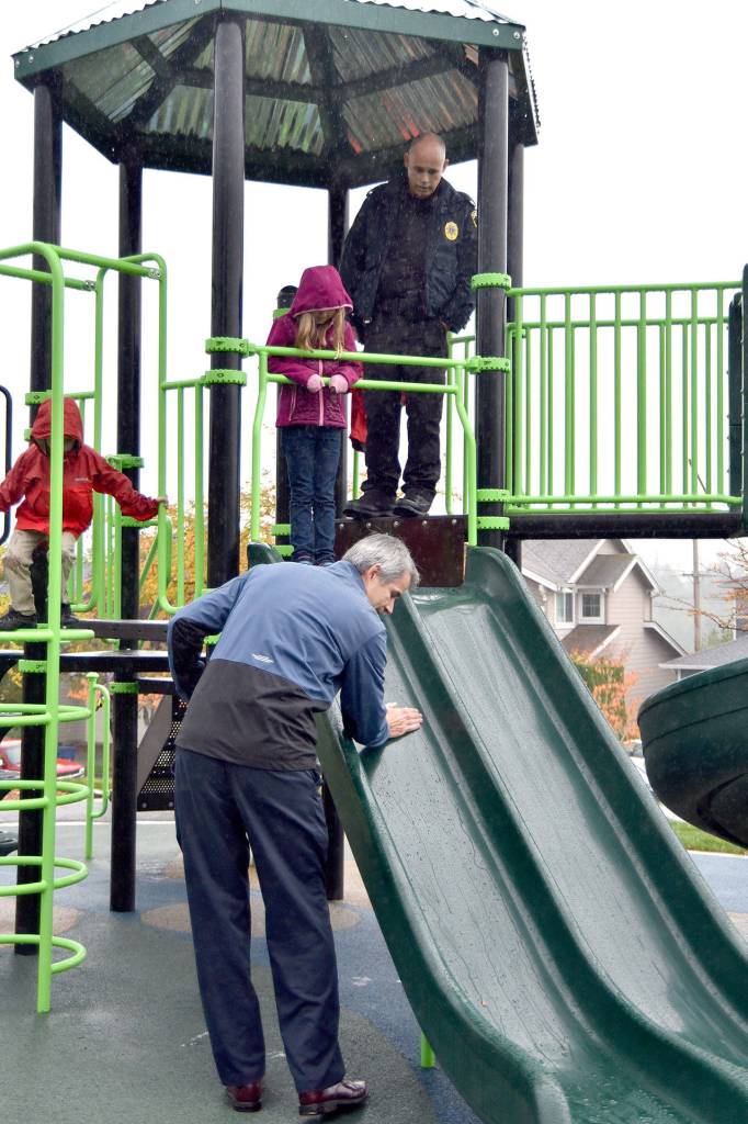 Mayor Matt Larson wipes down the slide so that the waiting Brielle Collins, or possibly Snoqualmie Police Chief Perry Phipps, can try out the new play equipment at Ironwood Park, despite the rain. (Carol Ladwig/Staff Photo)