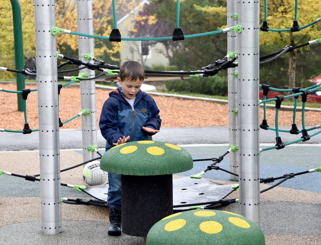 Nicholas Geib drums on the new Ironwood Park play structure in the rain, just before participants cut the ribbon to celebrate park improvements Wednesday, Oct. 25. (Carol Ladwig/Staff Photo)