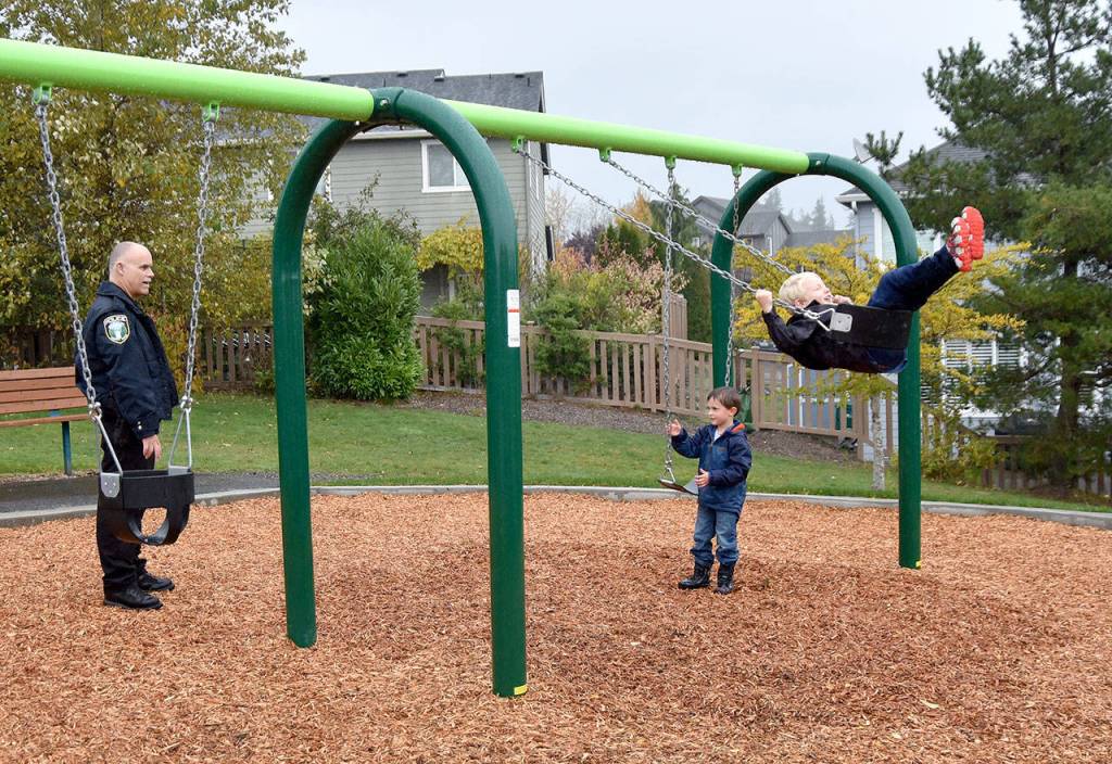 Snoqualmie Police Chief Perry Phipps watches as Mitchell Collins, left, and Nicholas Geib try out the new swingset at Ironwood Park. (Carol Ladwig/Staff Photo)