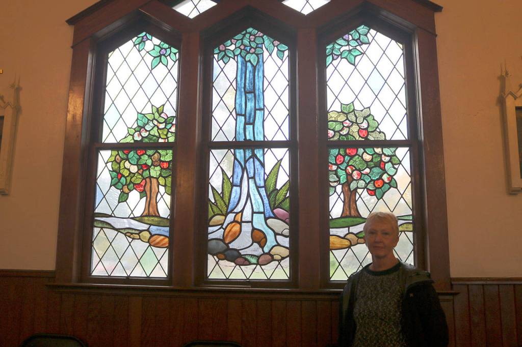 Tona McGuire stands with one of her favorite pieces in the church depicting Snoqualmie Falls and based on psalm 1:3. (Evan Pappas/Staff Photo)