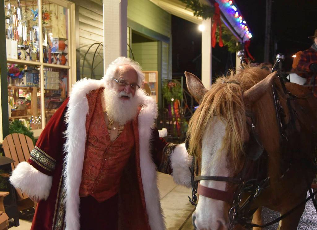 Father Christmas (left) greets one of the hard-working draft horses who pulled wagonloads of visitors through downtown Snoqualmie for hours Saturday during the citys holiday festivities. Sno Valley Winds musicians Erik Dickerson, center, and Erik Thurston performed for Saturdays tree lighting in Snoqualmie in holiday themed hats, the Grinch and Santa, respectively. (File Photo)