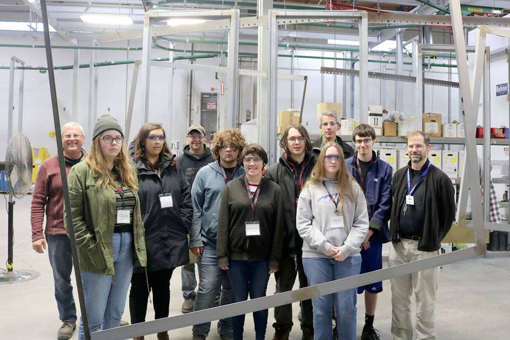 The first tour group poses for a group photo behind a large frame in the warehouse. From left: Tim Anderson, Clara Wallace, Isabel Jones, Daryl Petree, Elliot Kryger, Emberly Louwien, Gabe Thorne, Alex Otto, Snoqualmie Mayor Matt Larson, Tyler Grimm, Riku Smith.