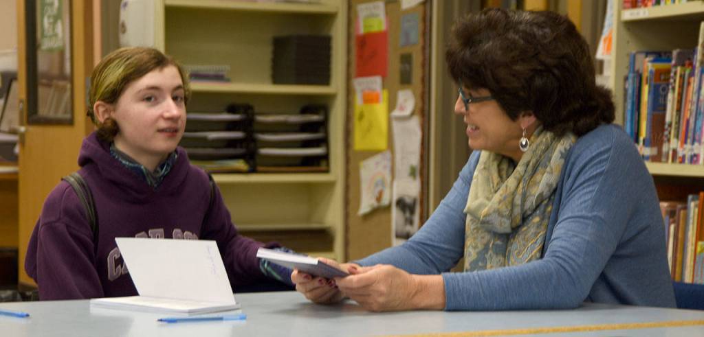 Sitting with her former teacher, first-time author Jay Dilger tells Marianne Bradburn about her work on the book she was donating signed copies of to the Opstad library. (Carol Ladwig/Staff Photo)