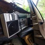 A boombox, in relatively good condition, is found wedged between the bare interior of a bus and two separated car doors. Photo by Caean Couto