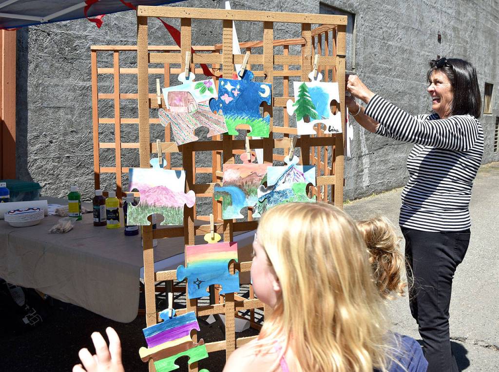 Susan OMalley hangs painted puzzle pieces to dry at the Mount Si Artist Guild booth Saturday during the Block Party. The pieces, painted by children as an arts activity, will be assembled into a community collage, OMalley said. Carol Ladwig/Staff Photo