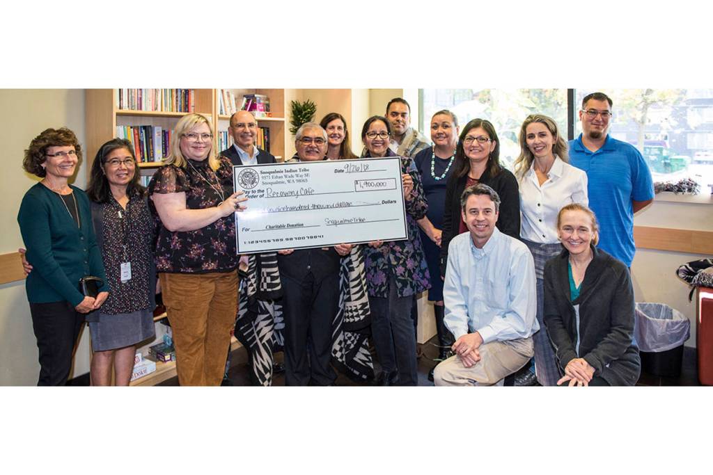 Elected members of the Snoqualmie Tribal Council meet with leaders from the Recovery Café to present a check for $1.9 million. From left, Debra Boyle, Ruby Takushi, Recovery Café co-founder, Alysse Bryson, Recovery Café Board vice chair, David Boyle, Recovery Café Board treasurer, Robert M. de los Angeles, Snoqualmie Tribal chairman, Vicki Allen, past board chair, Recovery Café, Diane Tomhave, past board chair, Recovery Café, Michael Ross, Snoqualmie Tribal vice chair, Suzanne Sailto, Snoqualmie Tribal Council, Jolene Williams, Snoqualmie Tribal secretary, David Coffey (kneeling, front) Recovery Café executive director, Rita Egrari, Recovery Café Board chair, Killian Noe (kneeling, front) Recovery Café founding director, Steve de los Angeles, Snoqualmie Tribal deputy secretary. Photo courtesy of the Snoqualmie Tribe.