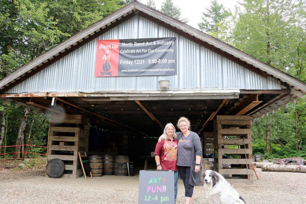 The 1924 train shed roof sits on the property as North Bend Art and Industry raises the money to rebuild the careful deconstructed and catalogued building. Debra Landers, left, and Beth Burrows prepared for the Summer kick off event with Landers dog Freyja on Saturday. Evan Pappas/Staff Photo