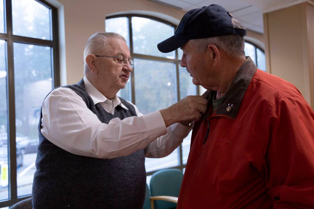 After a quick chat in the waiting room of the American Lake VA Medical Center, Jim Curtis, right, is given a small American flag pin by a fellow veteran. Curtis was there drawing attention to his fundraising efforts. Staff photos / Ashley Hiruko