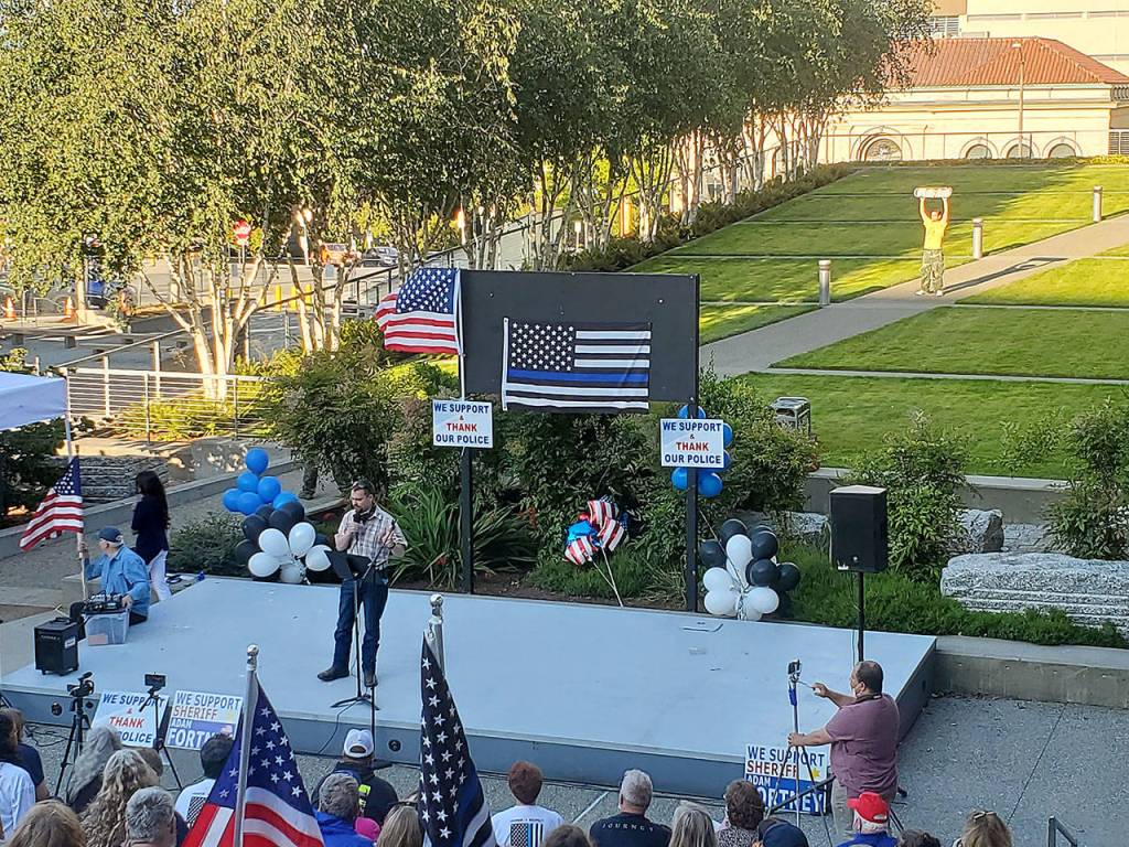 The man who was later arrested can be seen during the rally, behind the stage, holding up his skateboard in the sun. (Ian Davis-Leonard / The Herald)