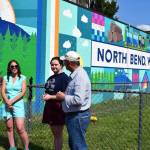 Sarah Hughes, left, unveils her mural in June alongside Ava Mulligan, a Two Rivers High School Student, and North Bend Mayor Rob McFarland. Photo by Conor Wilson/Valley Record.