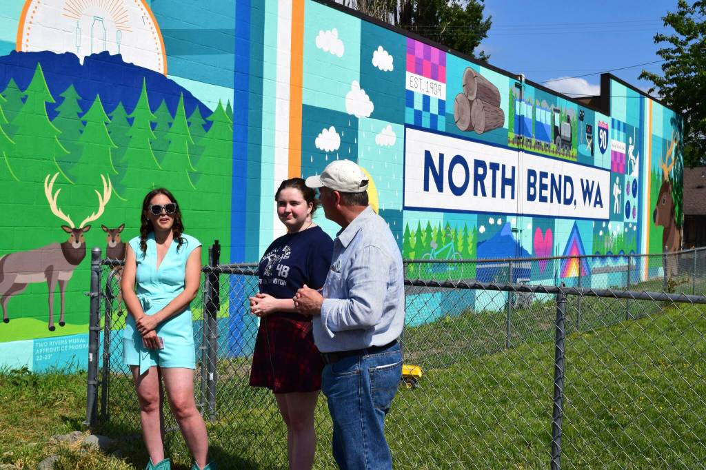 Sarah Hughes, left, unveils her mural in June alongside Ava Mulligan, a Two Rivers High School Student, and North Bend Mayor Rob McFarland. Photo by Conor Wilson/Valley Record.