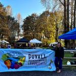 Duvall Farmers Market Board president Alex Yearout stands with the markets new banner on Oct. 3, 2024. (Grace Gorenflo/Valley Record)